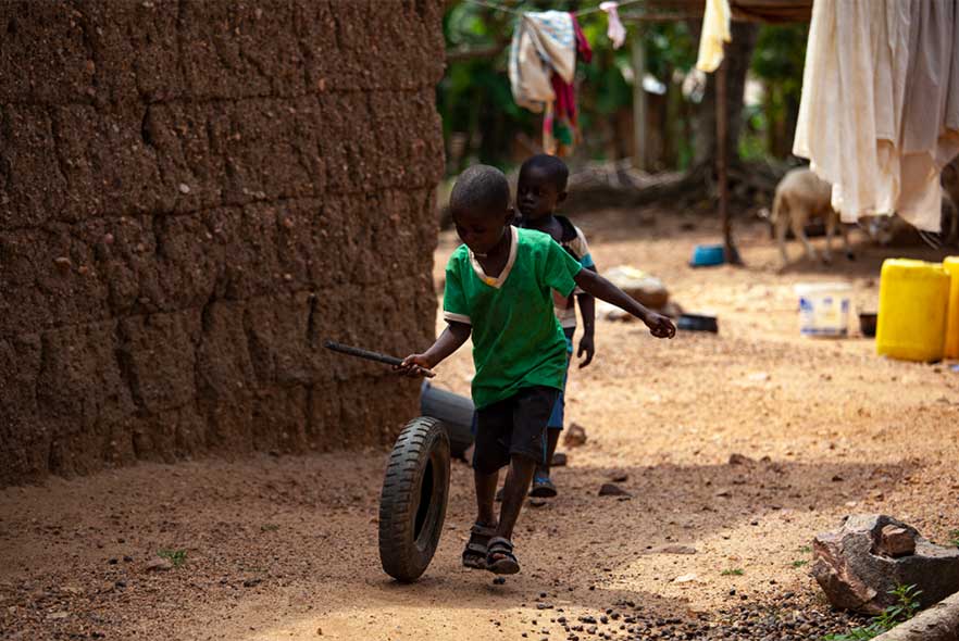 Boy in Ghana rolling a spare tyre with a stick 