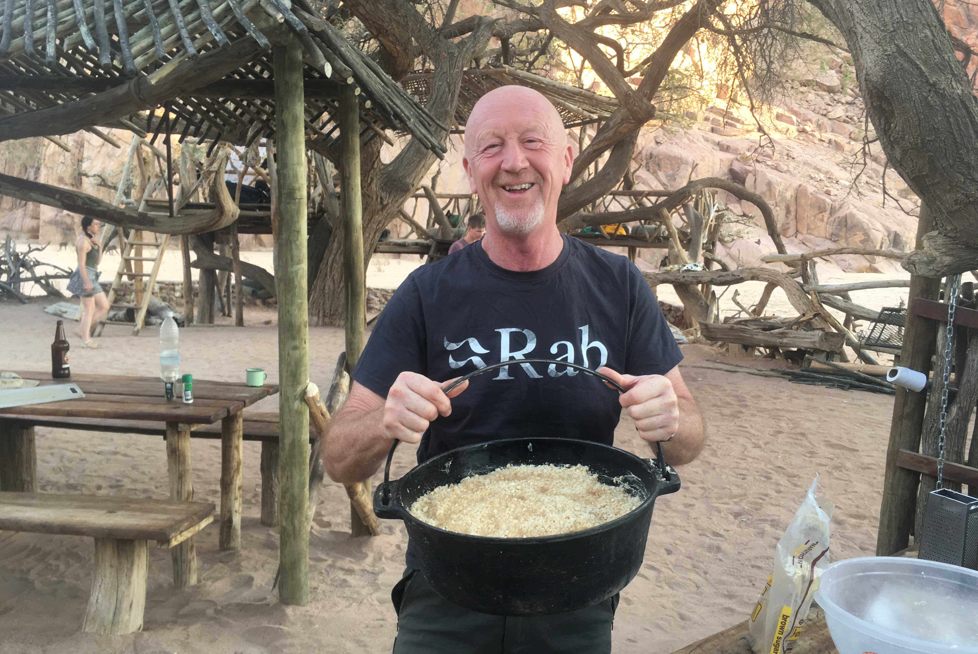 Retired volunteer cooking holding a pot of rice from an outdoor stove 