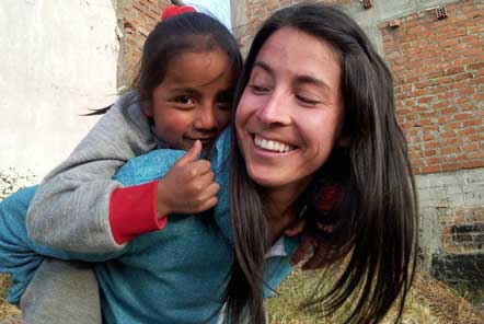 Lady volunteer giving a girl a piggy back and smiling as she gives a thumbs up