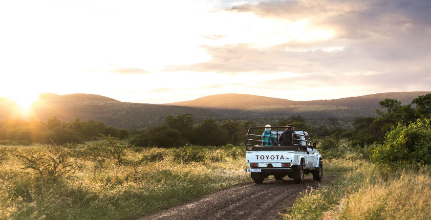 Volunteers in the back of a Toyota pick up truck driving on path in South Africa